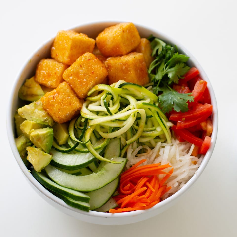 A GoPho bowl with crispy tofu, avocado, cucumber, zucchini, carrots, daikon, and tomatoes.