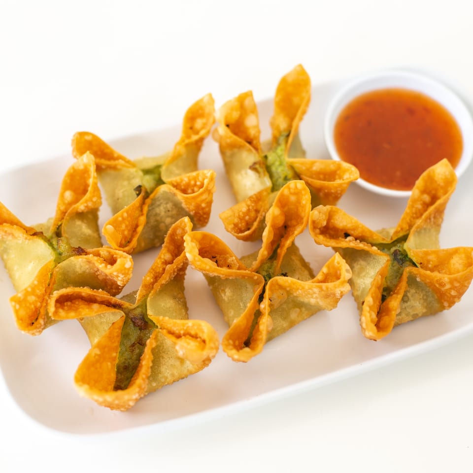 A white rectangular plate holds several golden-brown crab rangoon with a side of sweet chili sauce.