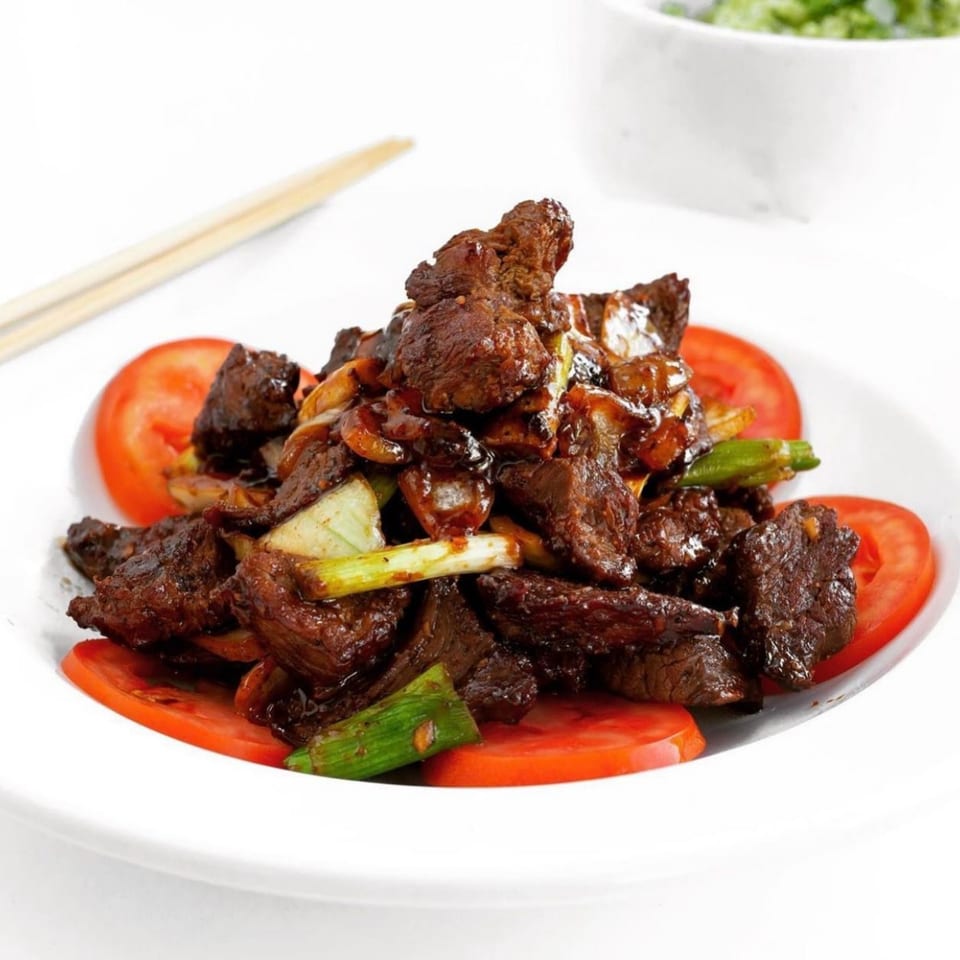 Shaking beef (Bò Lúc Lắc) with green onions and tomato slices on a white plate.