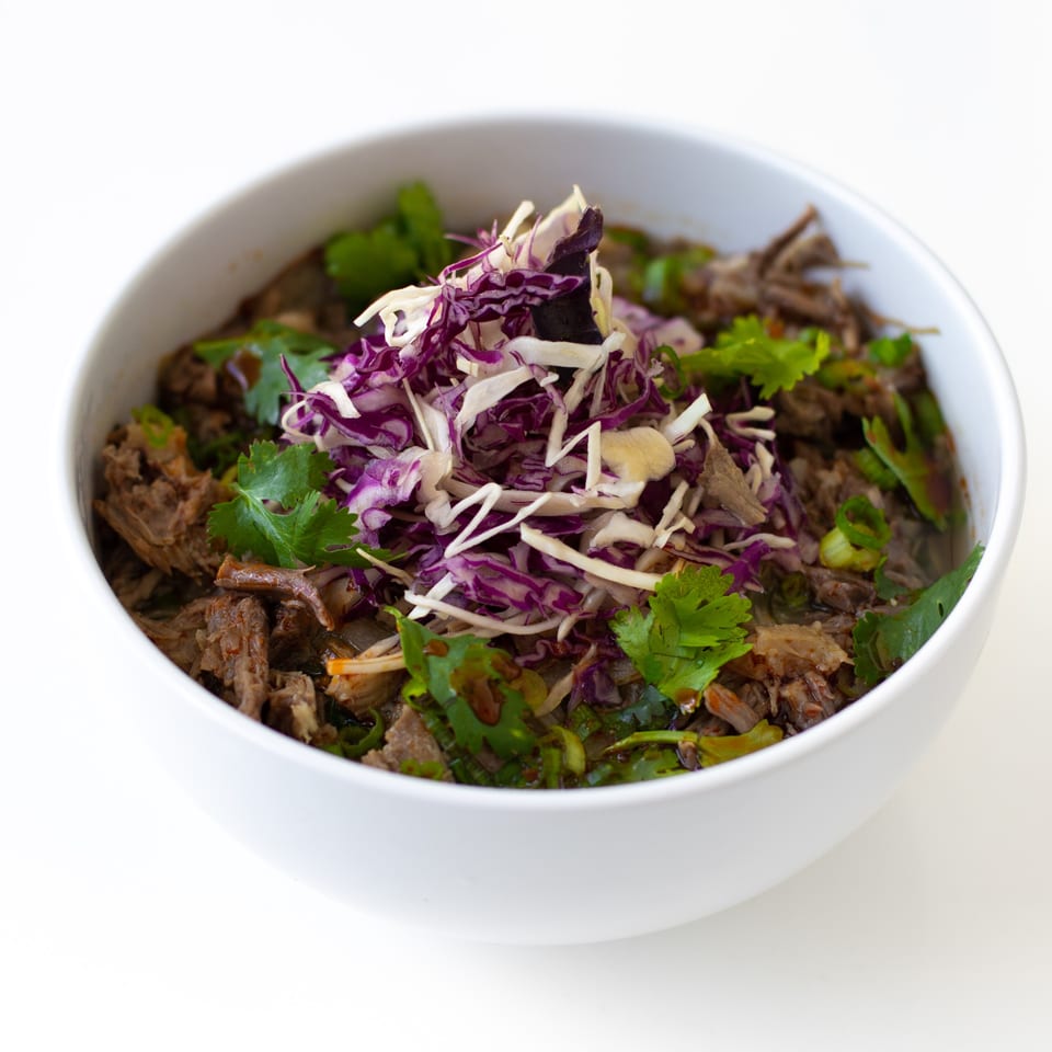 A white bowl filled with GoPho's Vietnamese shredded beef, topped with cilantro and shredded purple and white cabbage.