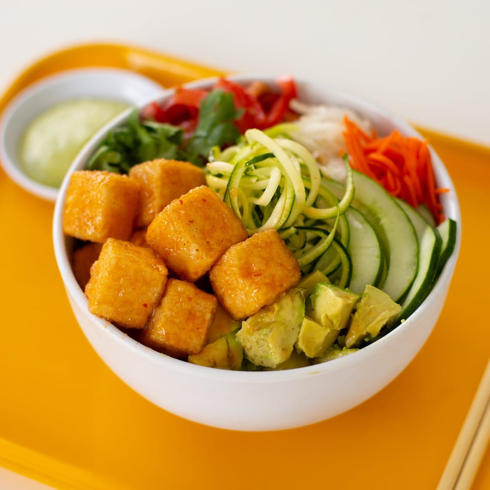 A GoPho tofu bowl with avocado, cucumber, zucchini, carrots, and cilantro on an orange tray.