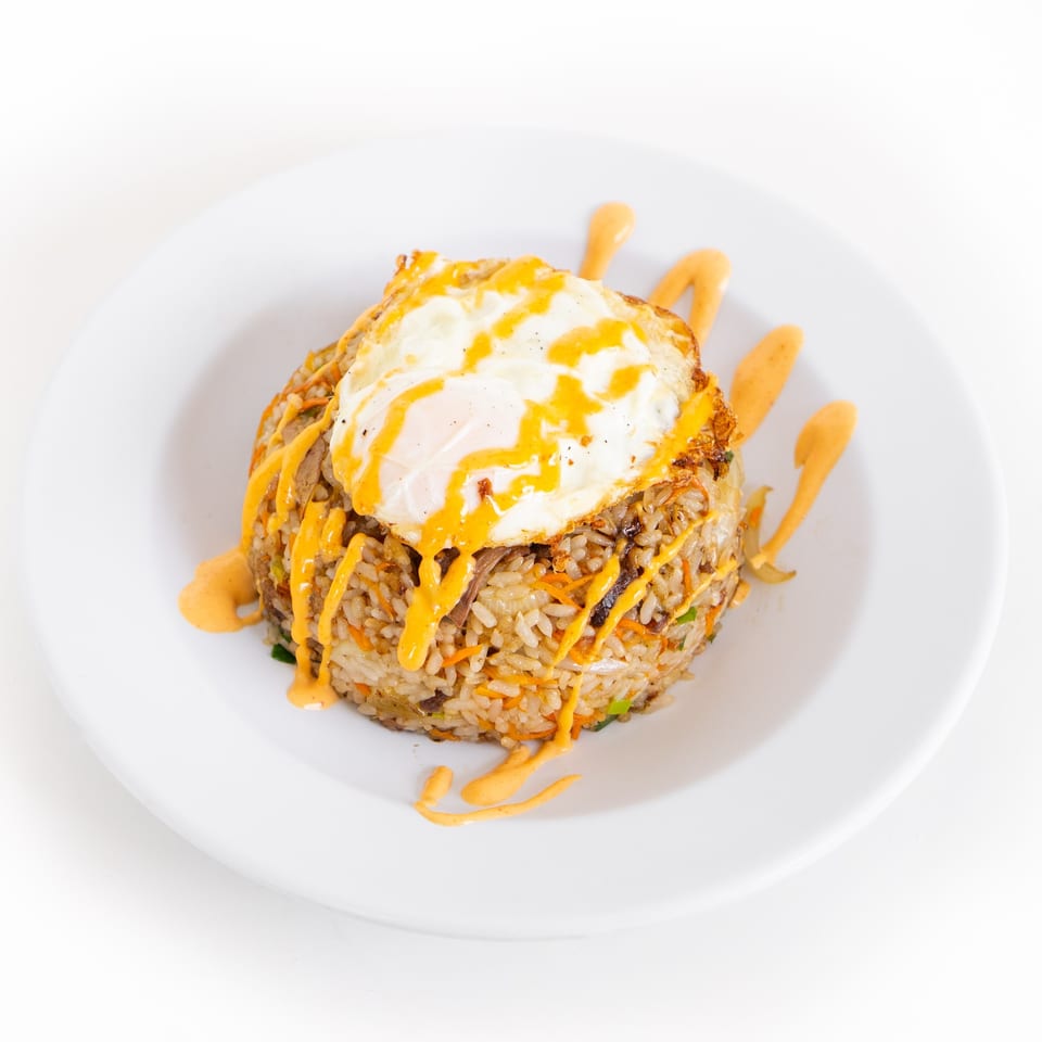 GoPho's fried rice topped with a sunny-side-up egg and drizzled with orange sauce on a white plate.