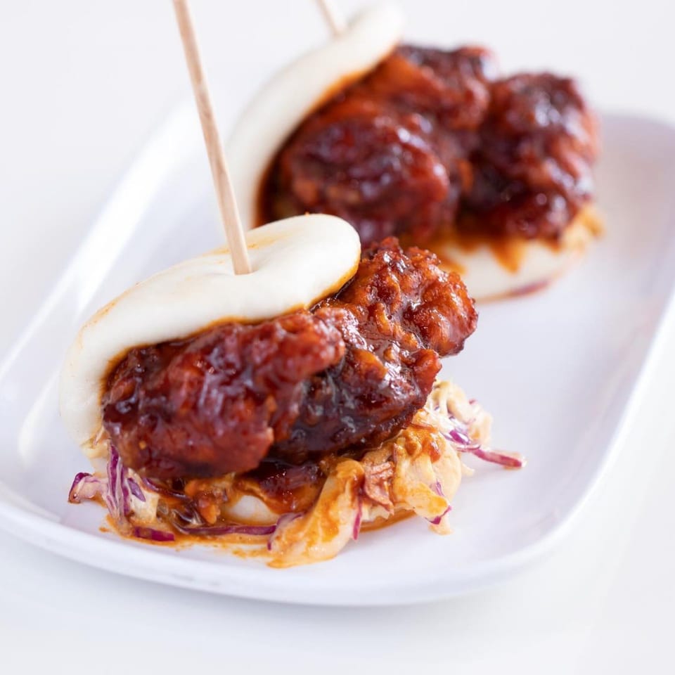 Two GoPho Vietnamese fried chicken bao buns with slaw on a white rectangular plate.