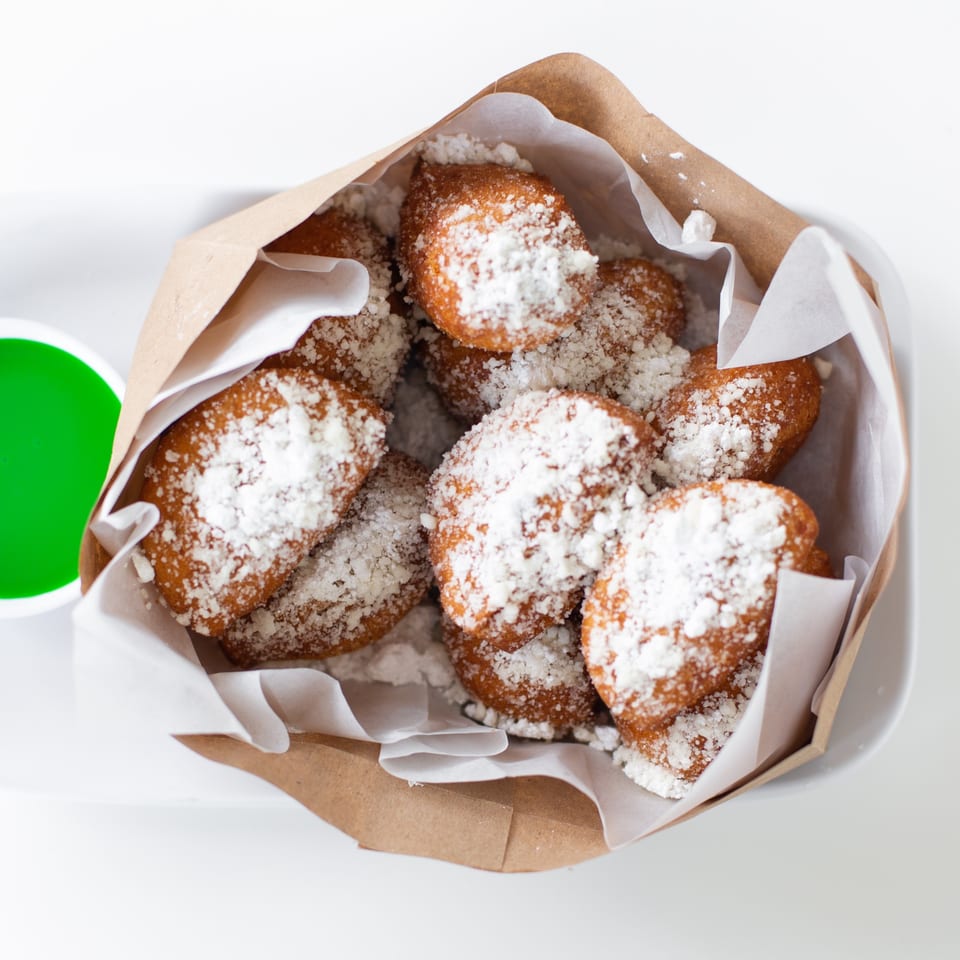 GoPho's Vietnamese donuts, golden brown and dusted with powdered sugar, in a brown paper bag with green dipping sauce.